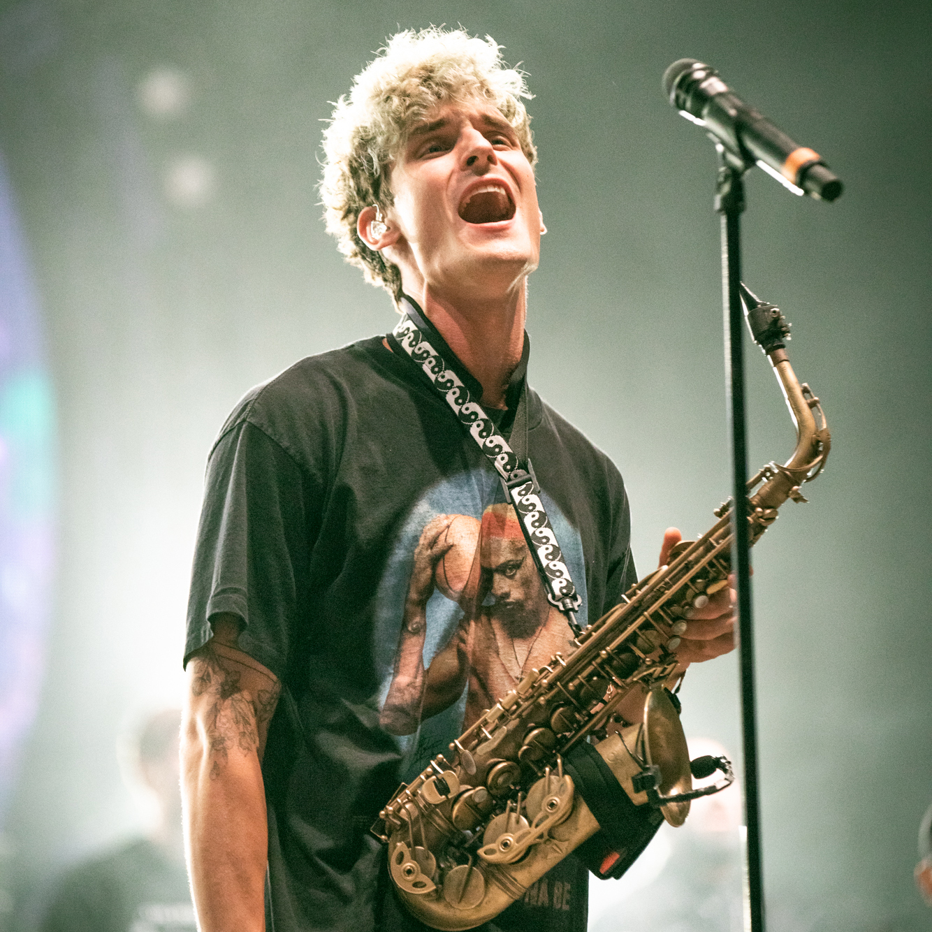 Musician GRiZ sings on stage with a saxophone around his neck