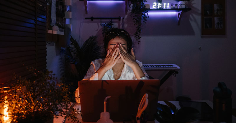 A woman puts her hands to her face working on her computer late at night