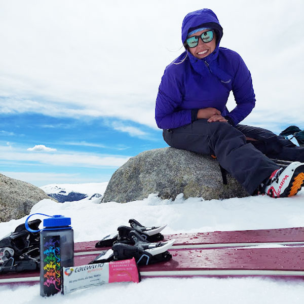 A student sitting on a rock in the snow with Tailwind Nutrition products in the foreground