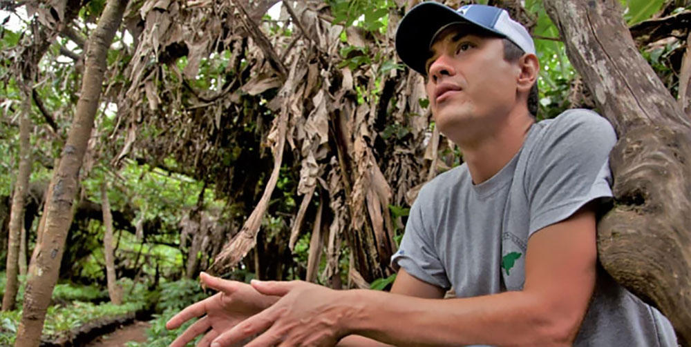 Sebastian Africano crouched down among trees in a Central American rural community