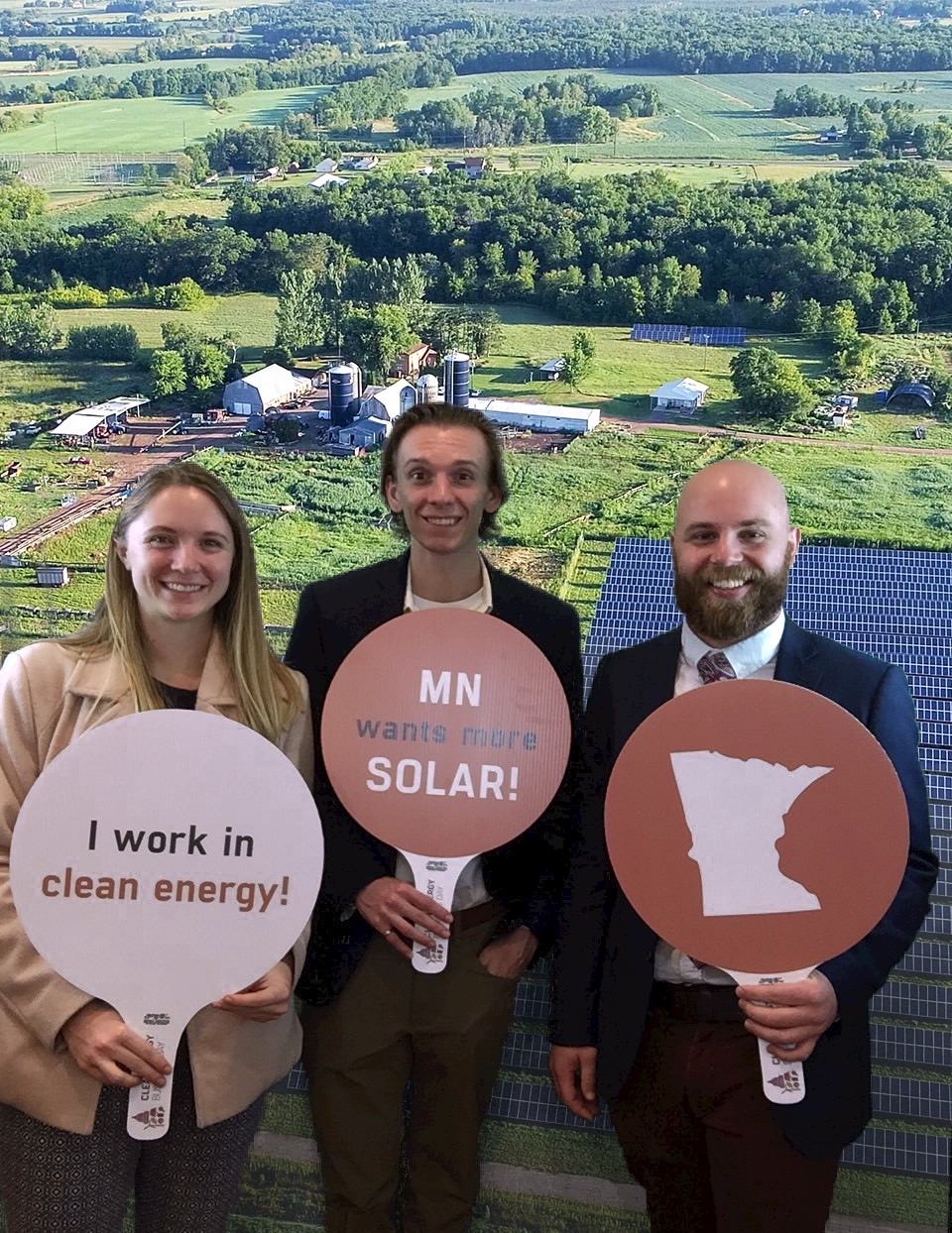 Addie Arnold stands with two men holding "I work in clean energy" signs
