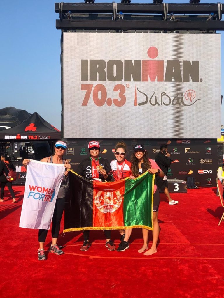 Zeinab and three others hold the Afghanistan flag in front of Ironman 70.3 Dubai sign