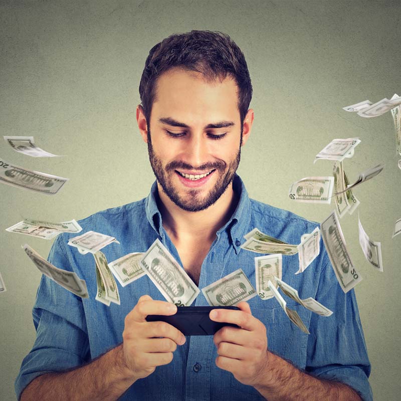 Image of a smiling man looking at a cell phone with money flying out from it.