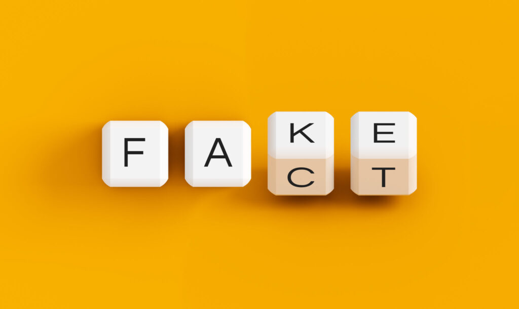 Four cubes against a yellow backdrop spelling out "fact" and "fake" with the last two cubes set askew to showcase both words.